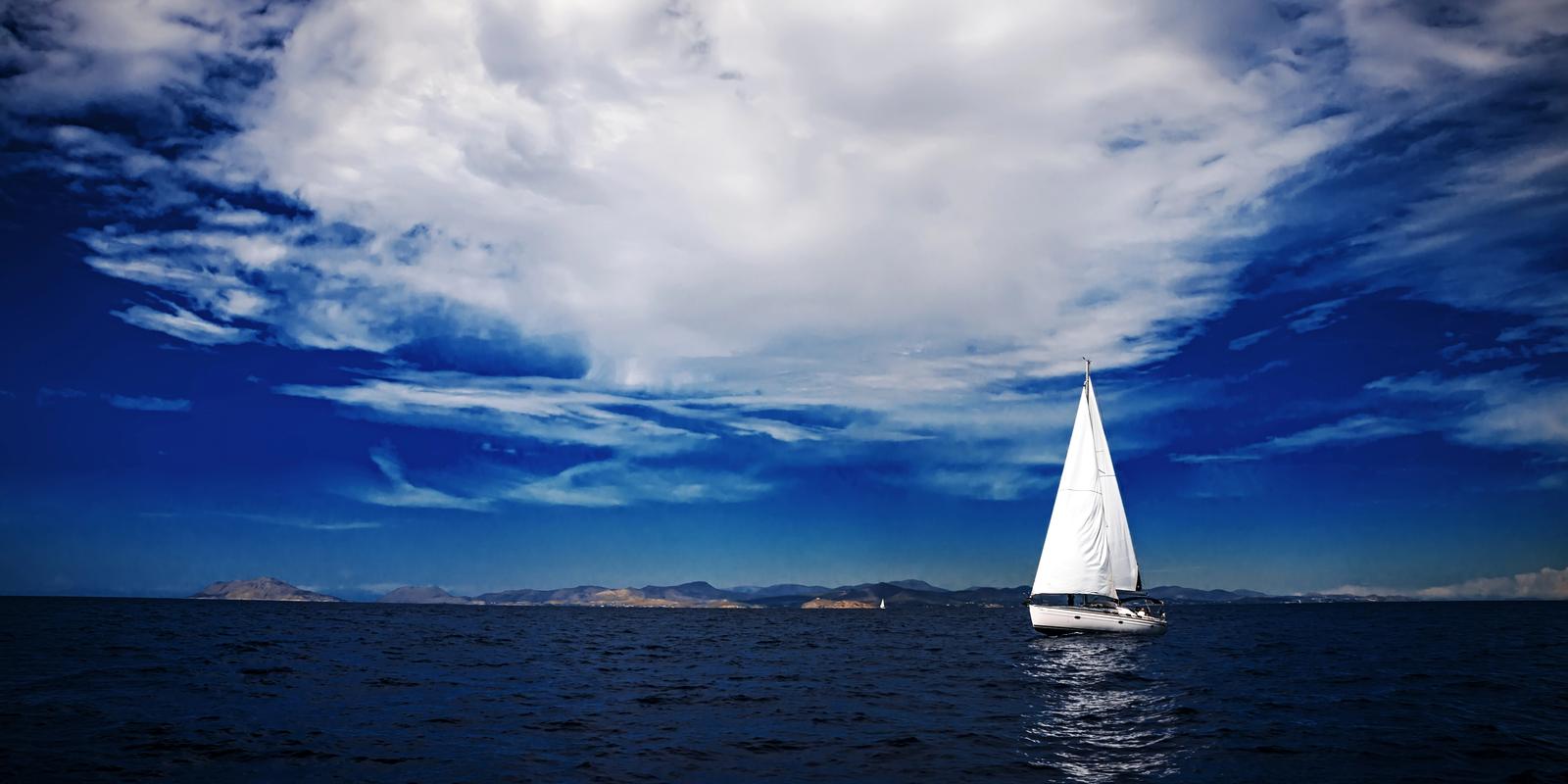 A lone sailboat on dark water under a towering white cloud