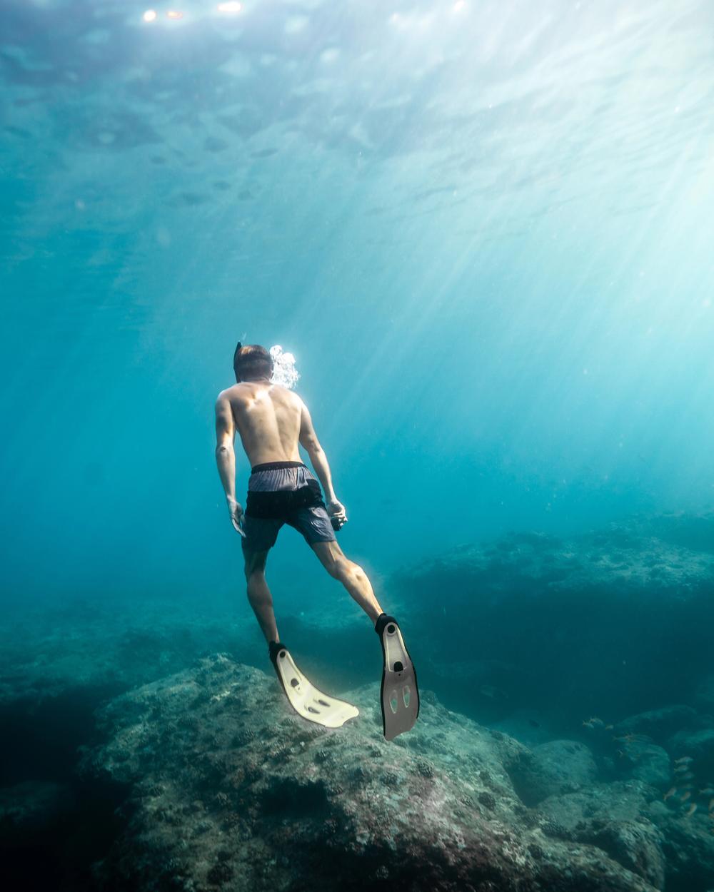 A freediver gliding down through shafts of light