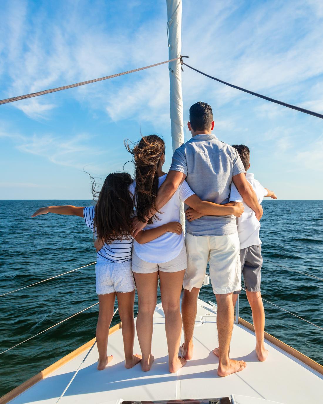A family standing together on the bow of a sailboat, looking out to sea