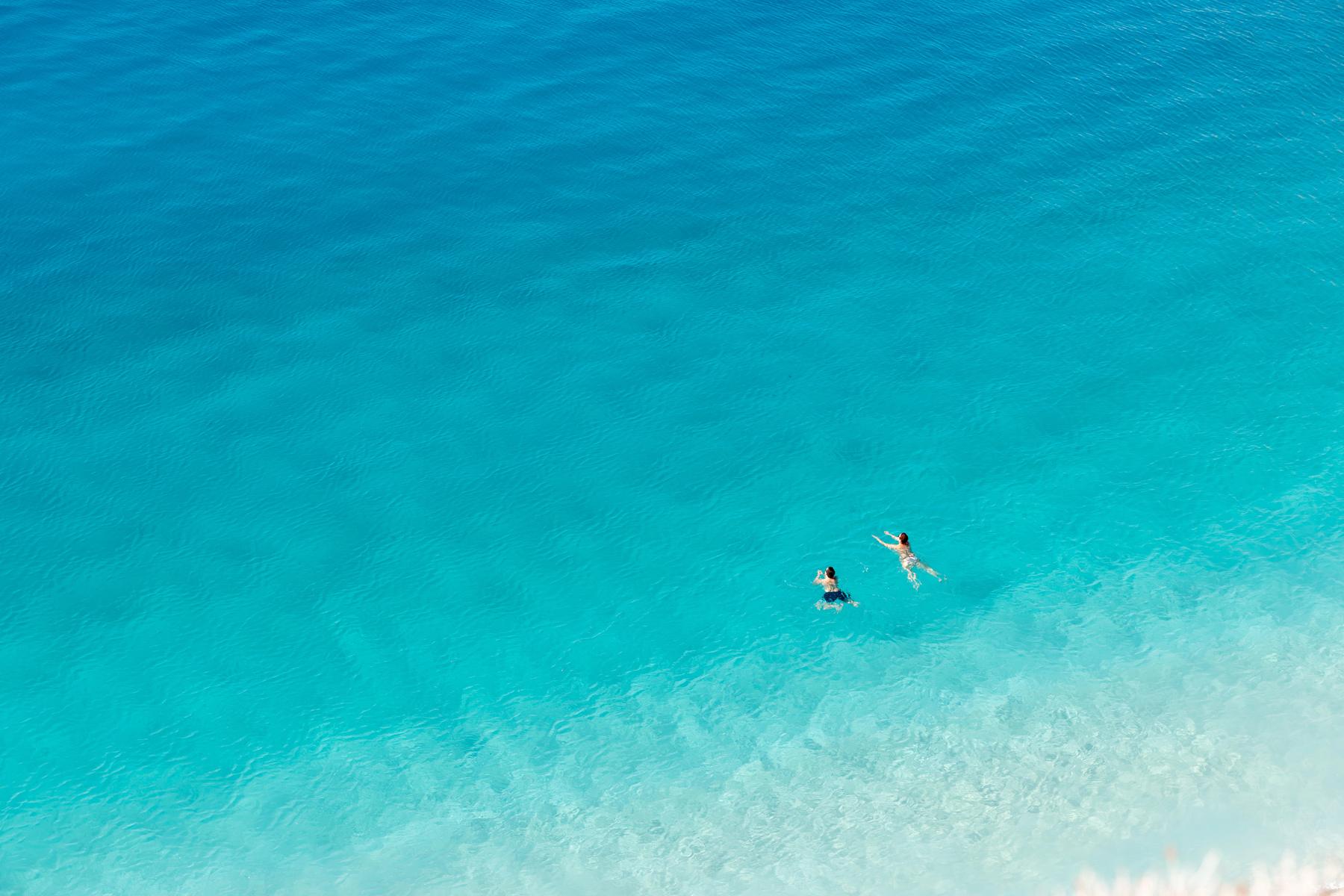 Two swimmers far out in clear turquoise water, seen from above