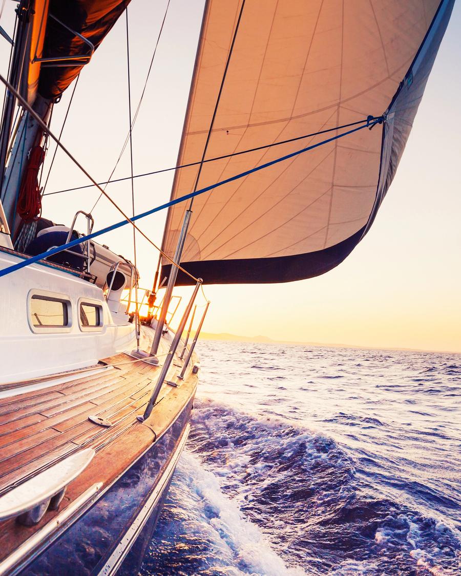 A sailboat heeled over under full sail at sunset