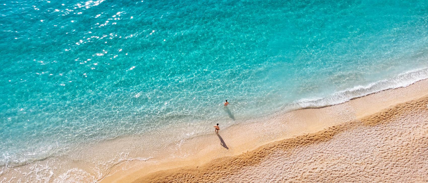 Two tiny figures walking along a long empty shoreline, seen from above