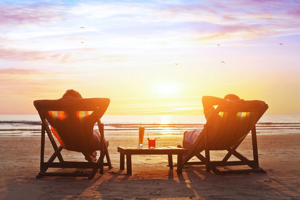 Two people relaxing in beach chairs at sunset, drinks on a small table between them
